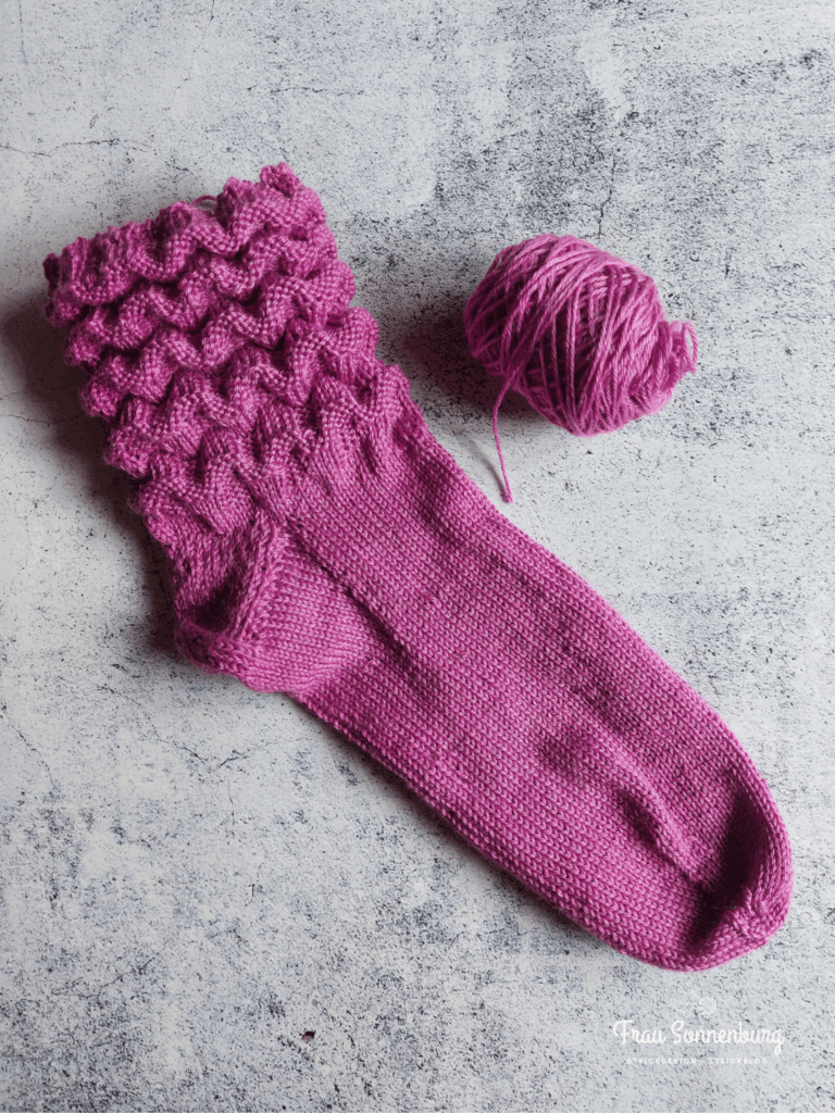 a pink sock with a ball of yarn - auf den Nadeln im Juli